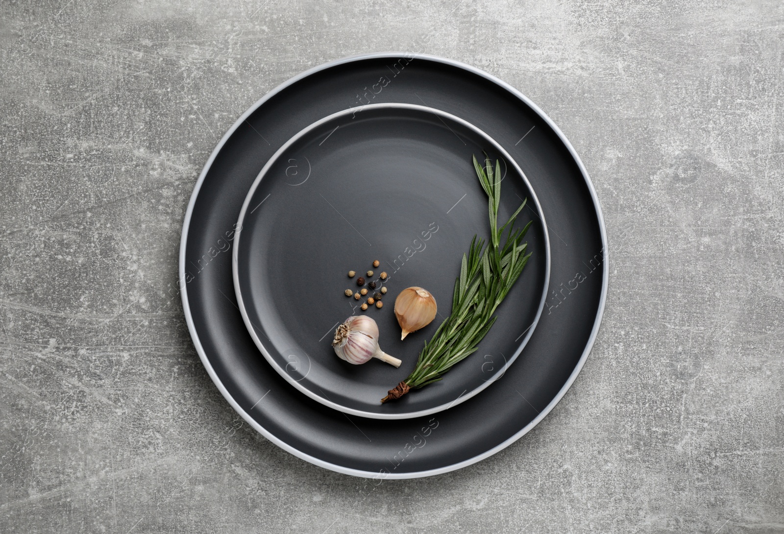 Photo of New dark plates with rosemary, garlic and peppercorns on light grey table, top view