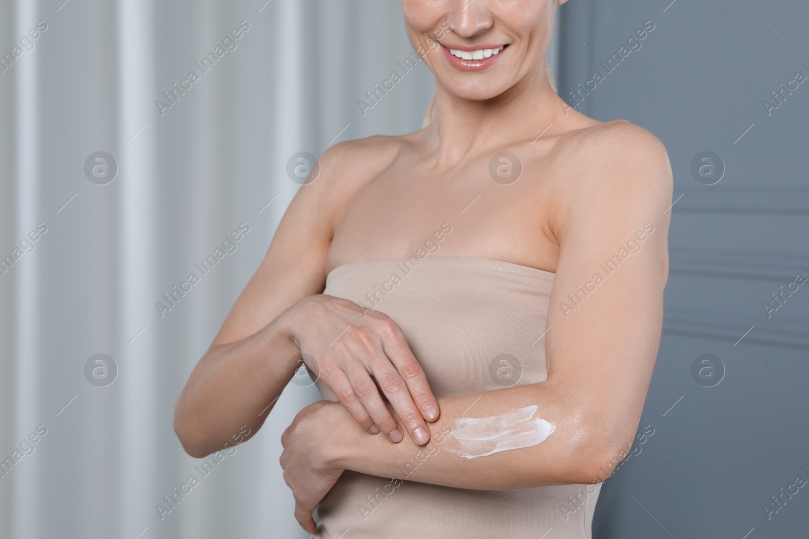 Photo of Woman applying body cream onto arm indoors, closeup. Space for text