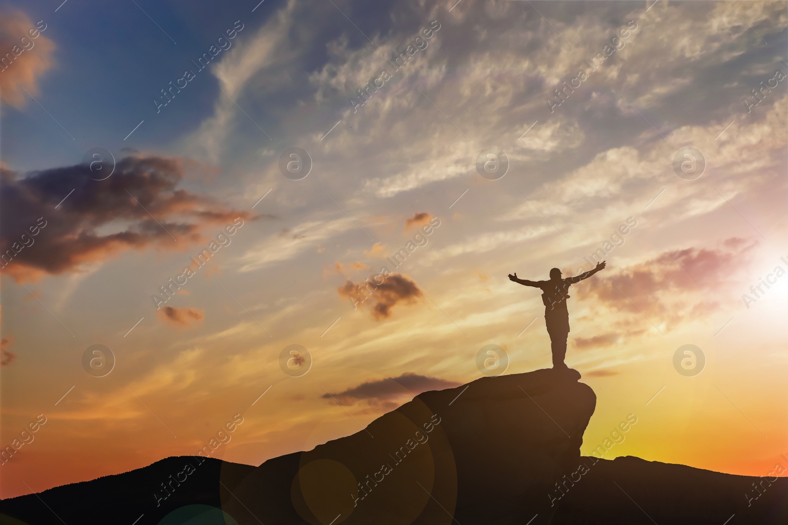 Image of Silhouette of man on peak at sunset. Space for text