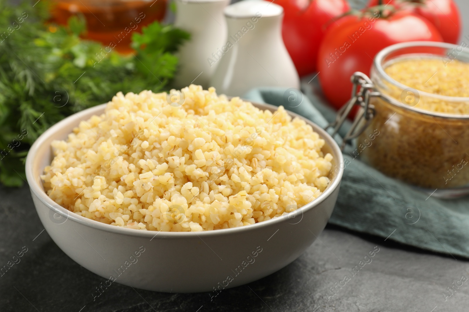 Photo of Delicious bulgur in bowl on black table, closeup