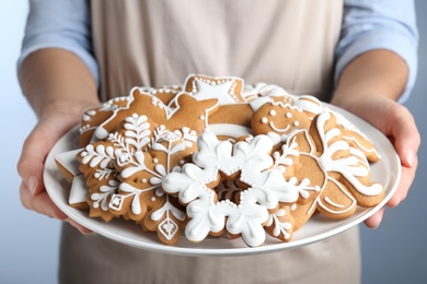 Photo of Woman with plate of delicious gingerbread Christmas cookies on grey background, closeup