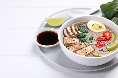 Delicious vegetarian ramen in bowl and soy sauce on white table. Space for text