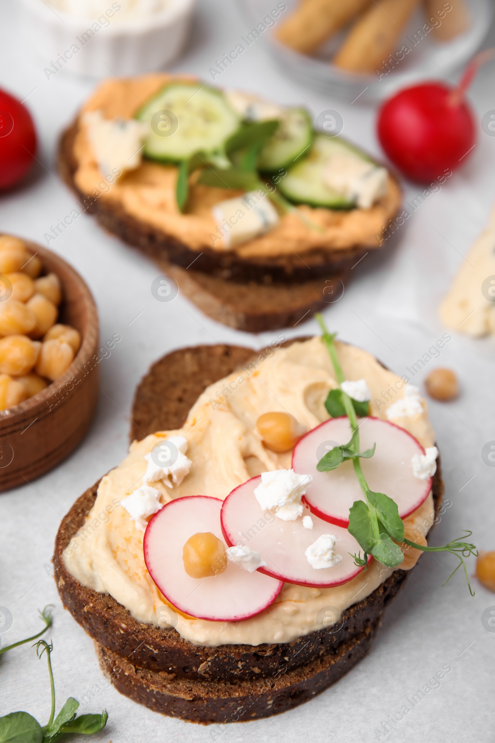 Photo of Delicious sandwiches with hummus and ingredients on light grey table