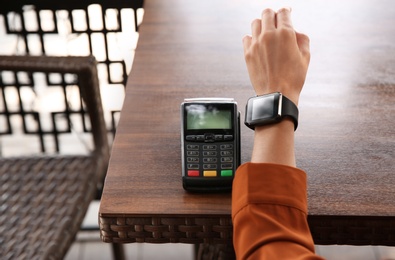 Photo of Woman making payment with smart watch at table, closeup