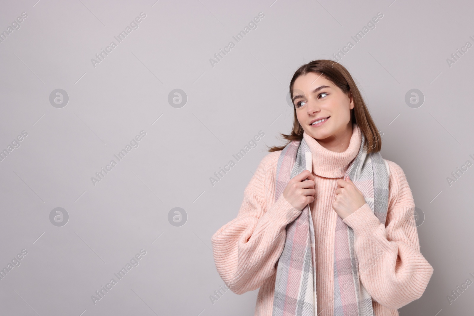 Photo of Beautiful woman in warm scarf on gray background, space for text