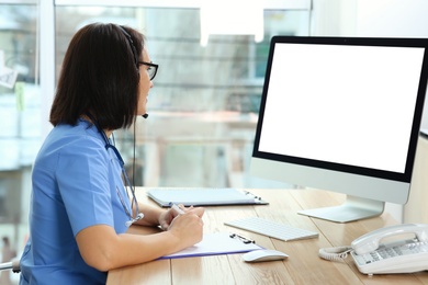 Photo of Doctor with headset and computer consulting patient online in office. Hotline service