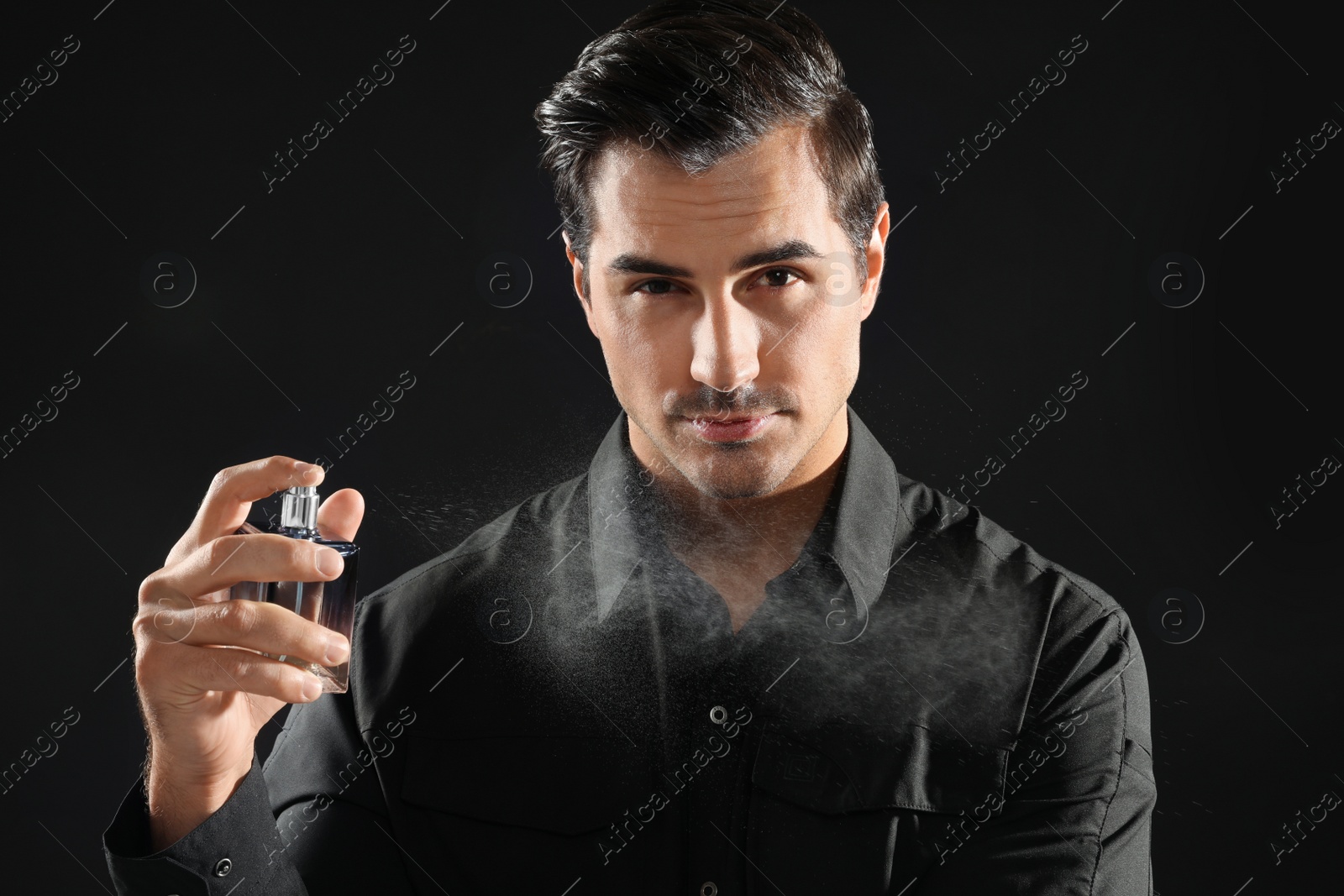 Photo of Handsome young man spraying perfume on black background