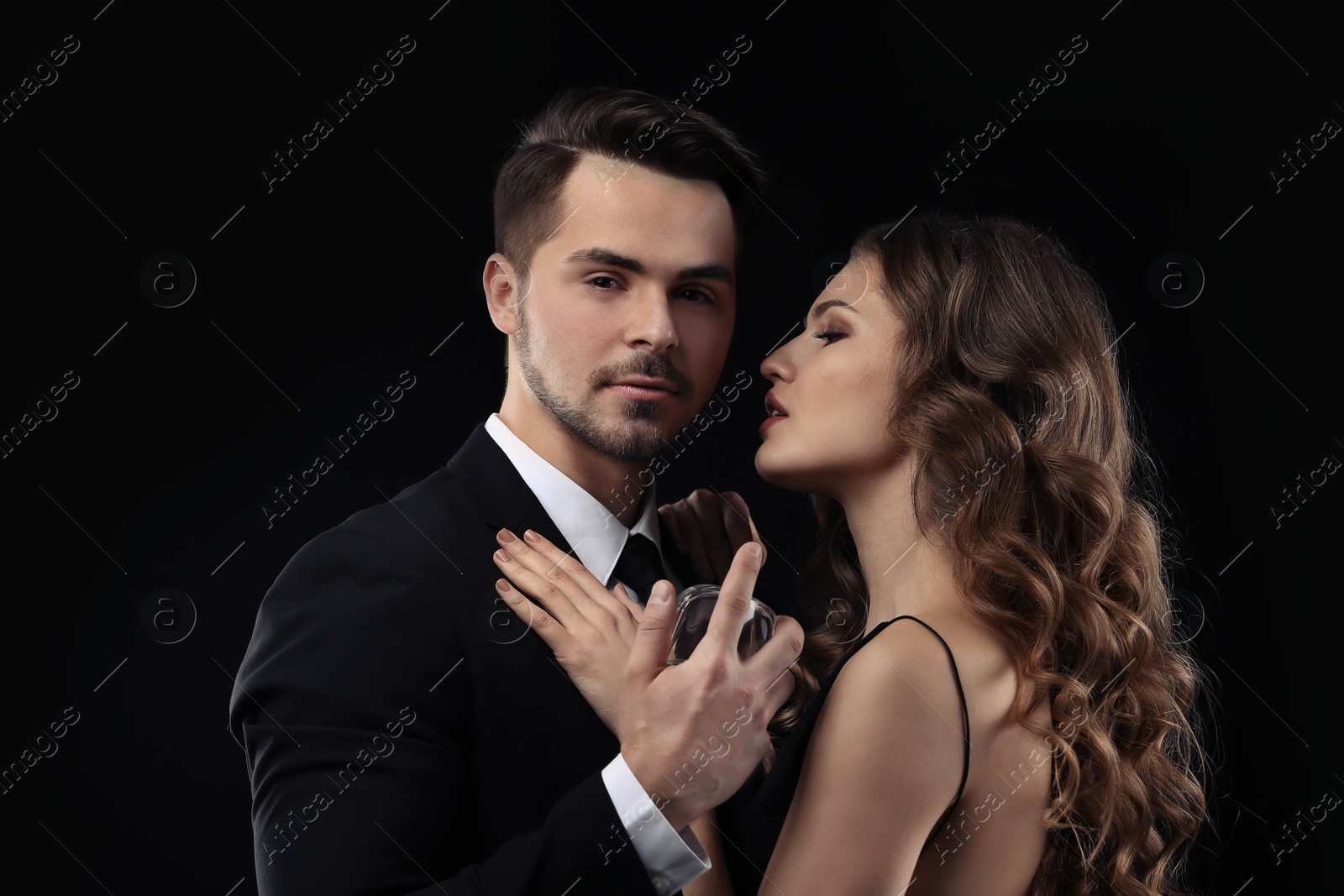 Photo of Passionate woman and handsome man using perfume on black background