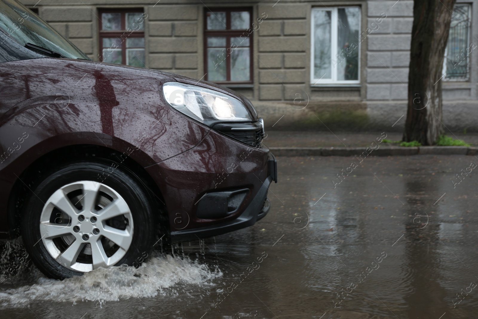Photo of Car driving through large puddle outdoors on rainy day