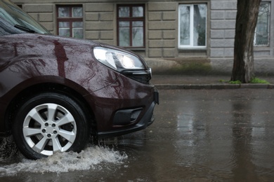 Car driving through large puddle outdoors on rainy day