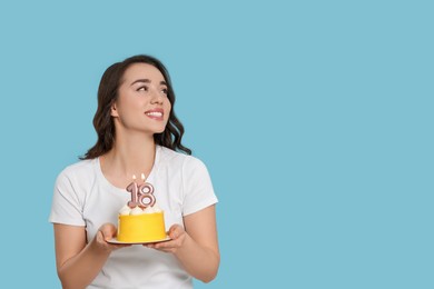 Coming of age party - 18th birthday. Woman holding delicious cake with number shaped candles on light blue background, space for text