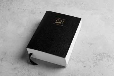 Photo of Bible with black cover on light gray table. Christian religious book