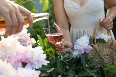 Women with bottle and glass of rose wine in peony garden, closeup