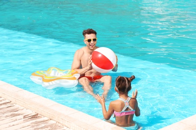 Happy father and little daughter playing with inflatable ball in swimming pool