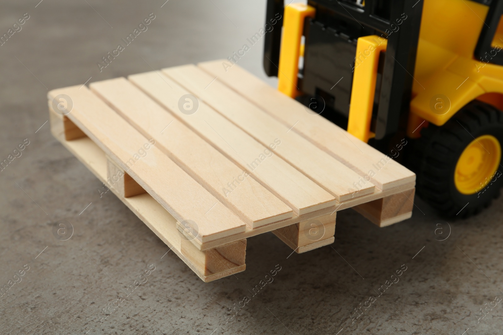 Photo of Toy forklift with wooden pallet on light grey table, closeup