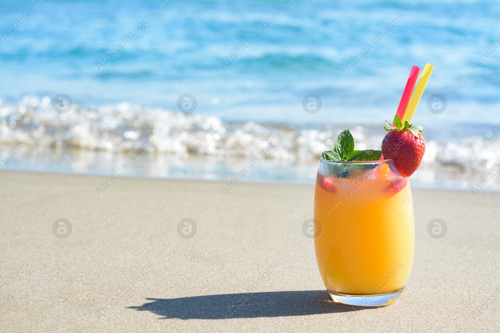 Photo of Glass of refreshing drink with strawberry on sandy beach near sea, space for text