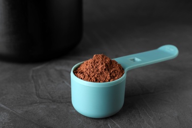 Photo of Scoop of chocolate protein powder on grey stone table