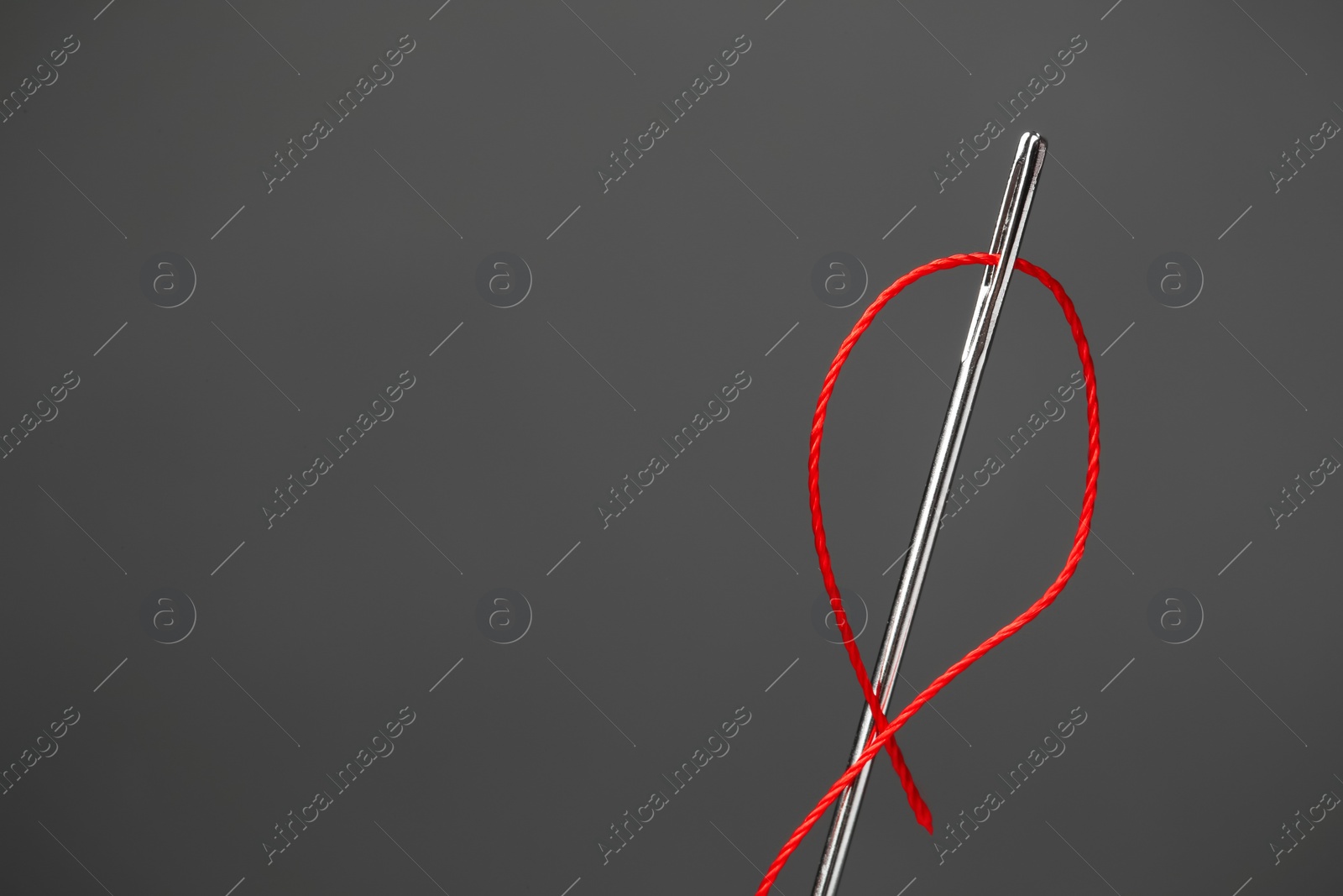 Photo of Needle with sewing thread on dark background, closeup