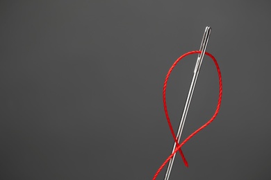 Photo of Needle with sewing thread on dark background, closeup