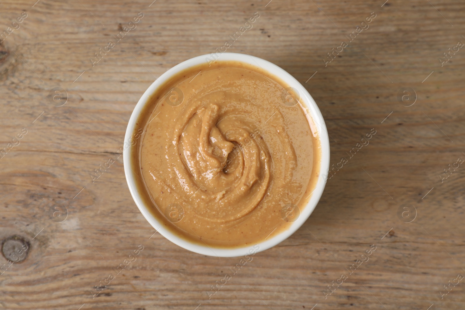 Photo of Delicious nut butter in bowl on wooden table, top view