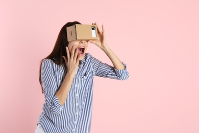 Young woman using cardboard virtual reality headset on color background. Space for text