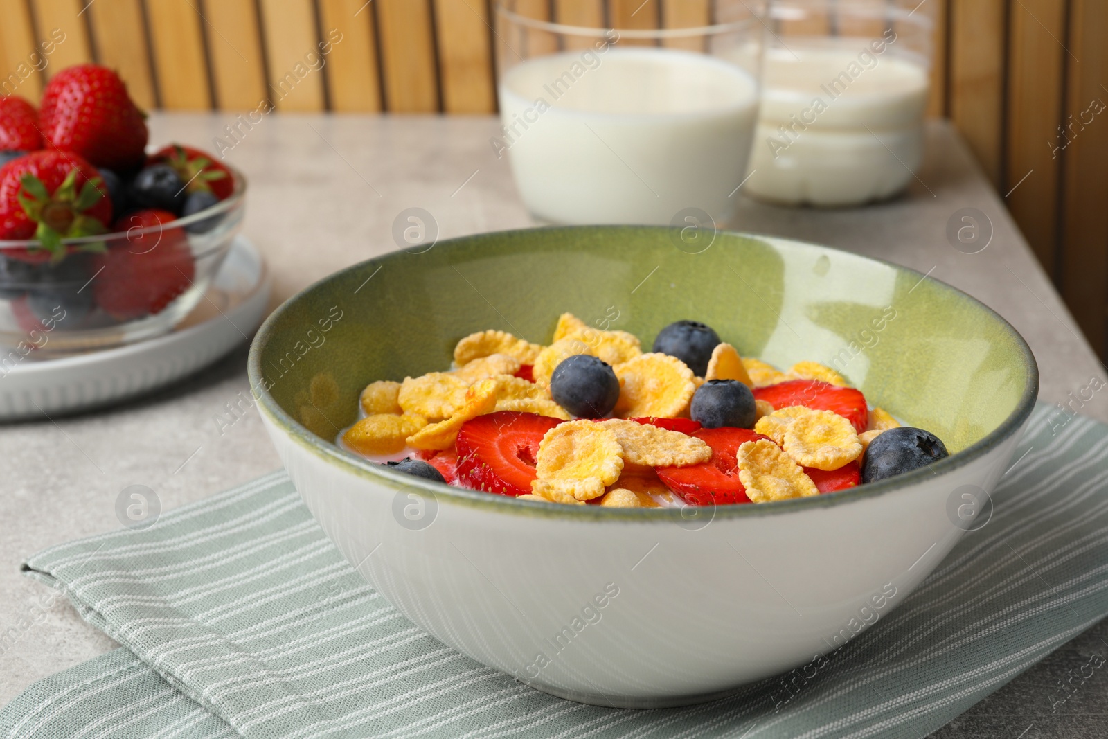 Photo of Corn flakes with berries in bowl served on grey table, closeup