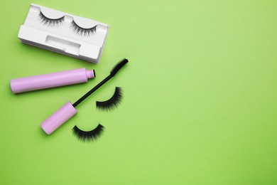 Photo of Flat lay composition with fake eyelashes and mascara brush on green background. Space for text
