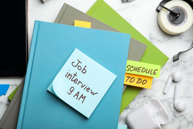 Reminder note about job interview and stationery on table, flat lay