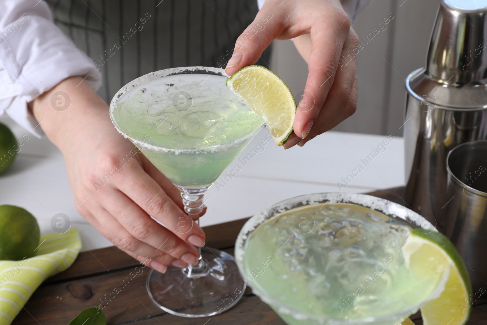 Photo of Bartender putting piece of lime onto glass with delicious Margarita cocktail at wooden table, closeup