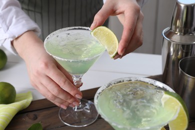 Bartender putting piece of lime onto glass with delicious Margarita cocktail at wooden table, closeup