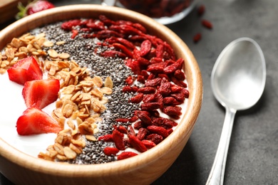 Photo of Smoothie bowl with goji berries and spoon on grey table, closeup