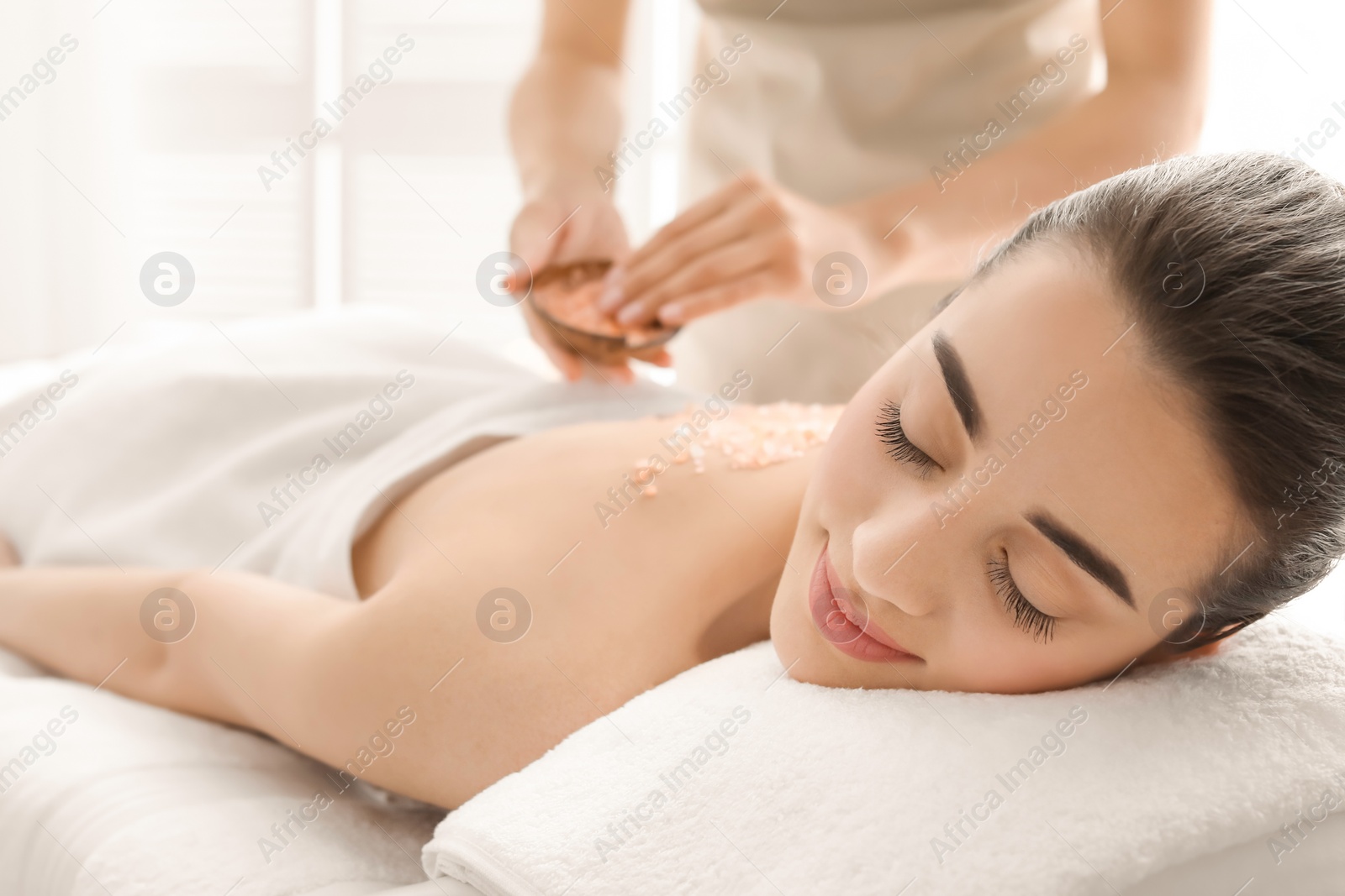 Photo of Young woman having body scrubbing procedure with sea salt in spa salon