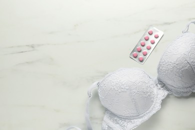 Photo of Breast cancer awareness. Bra and pills on white marble table, flat lay. Space for text