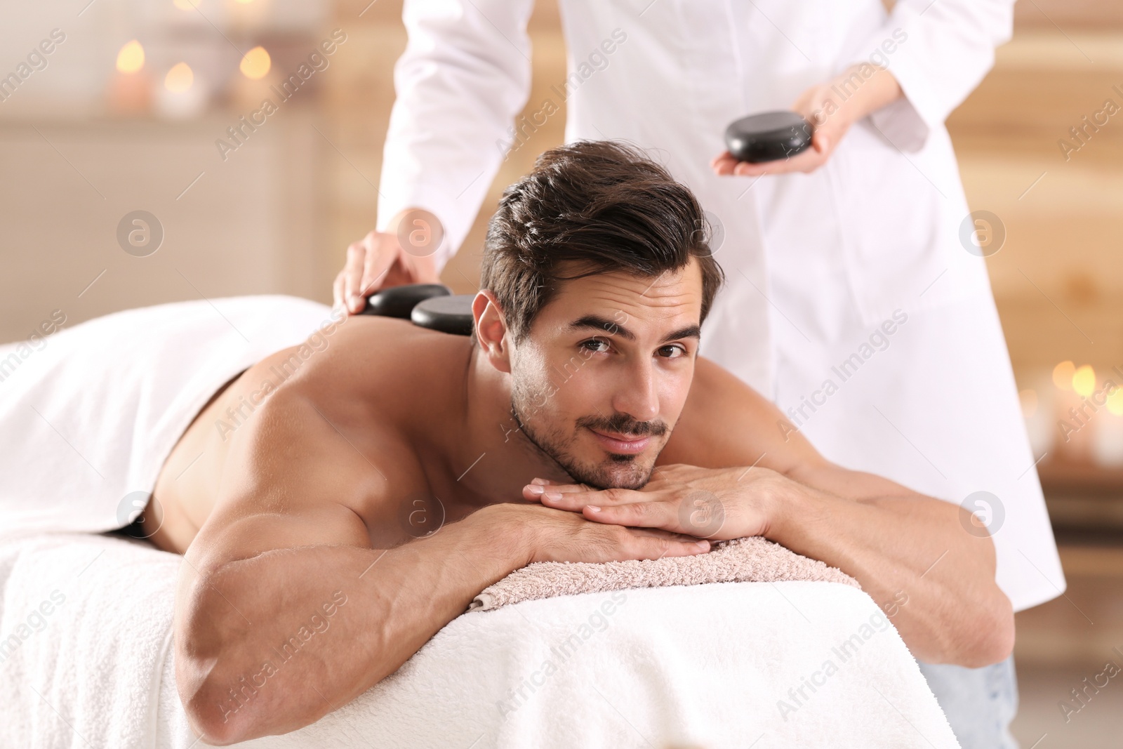 Photo of Handsome young man receiving hot stone massage in spa salon