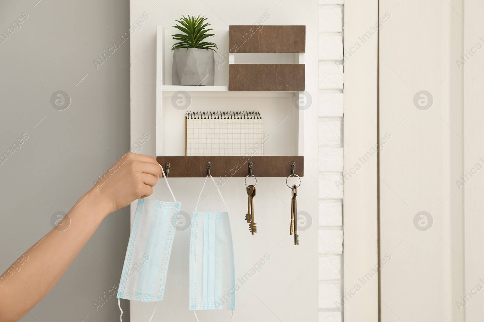 Photo of Woman taking protective mask from key hanger in hallway, closeup