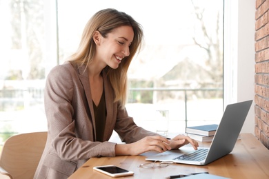 Photo of Young businesswoman using laptop at table in office