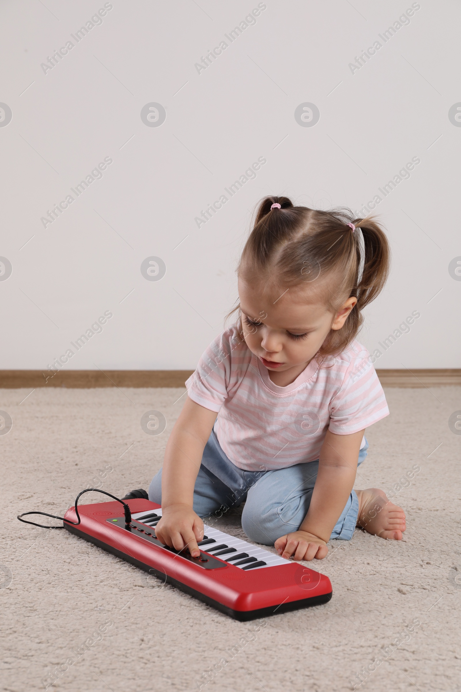 Photo of Cute little girl playing with toy piano at home