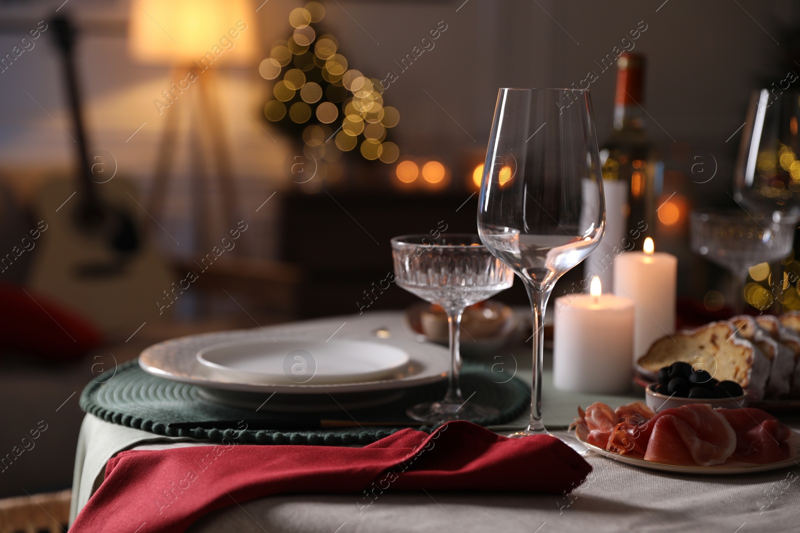 Photo of Christmas table setting with burning candles, appetizers and dishware indoors