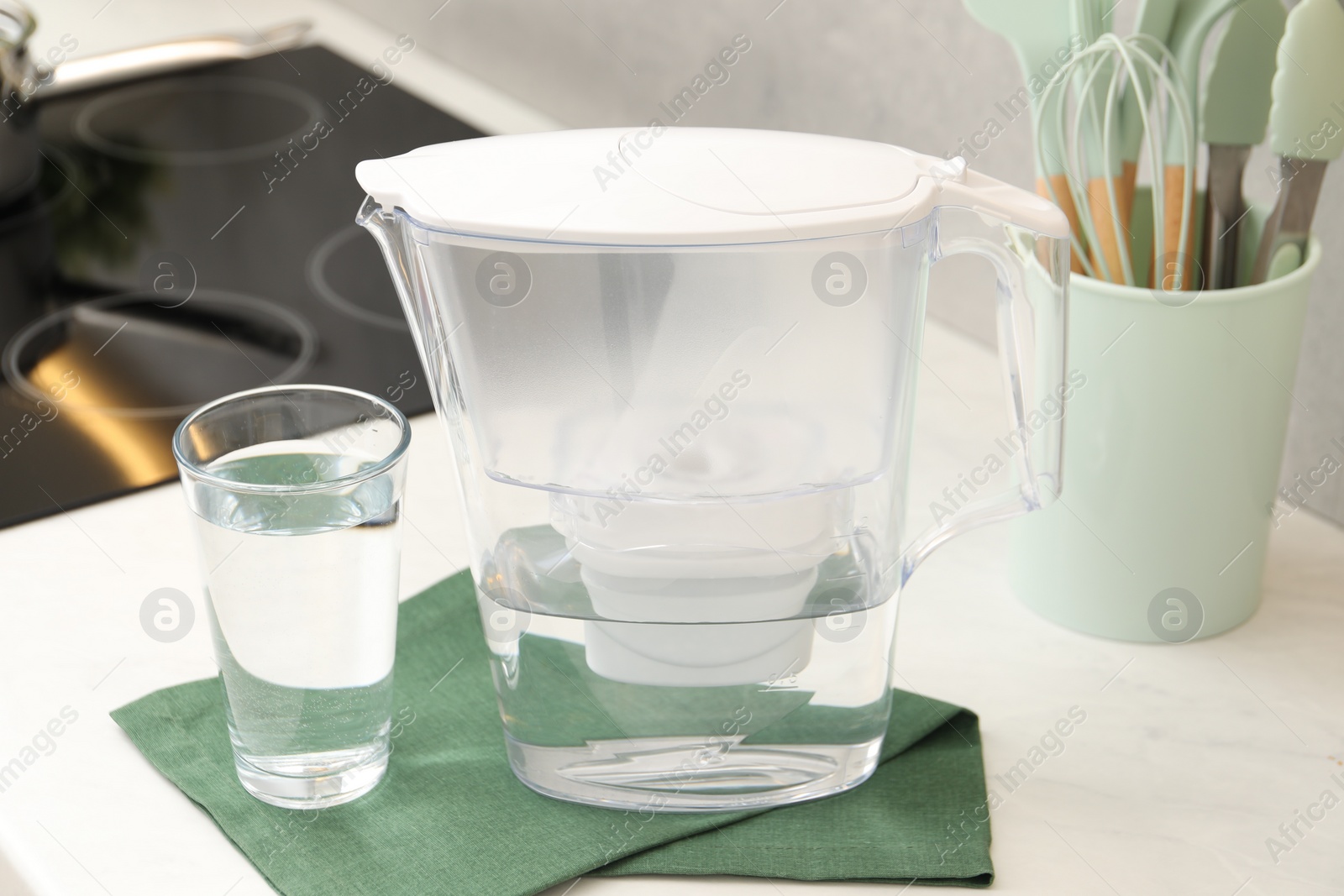 Photo of Water filter jug and glass on white countertop in kitchen