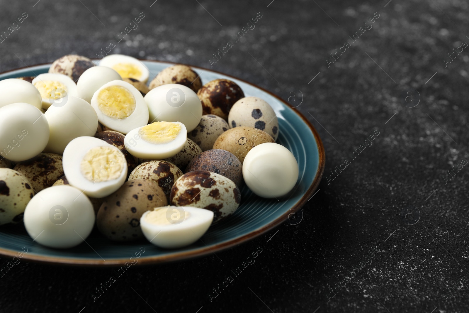 Photo of Peeled and unpeeled hard boiled quail eggs in plate on black table, closeup. Space for text