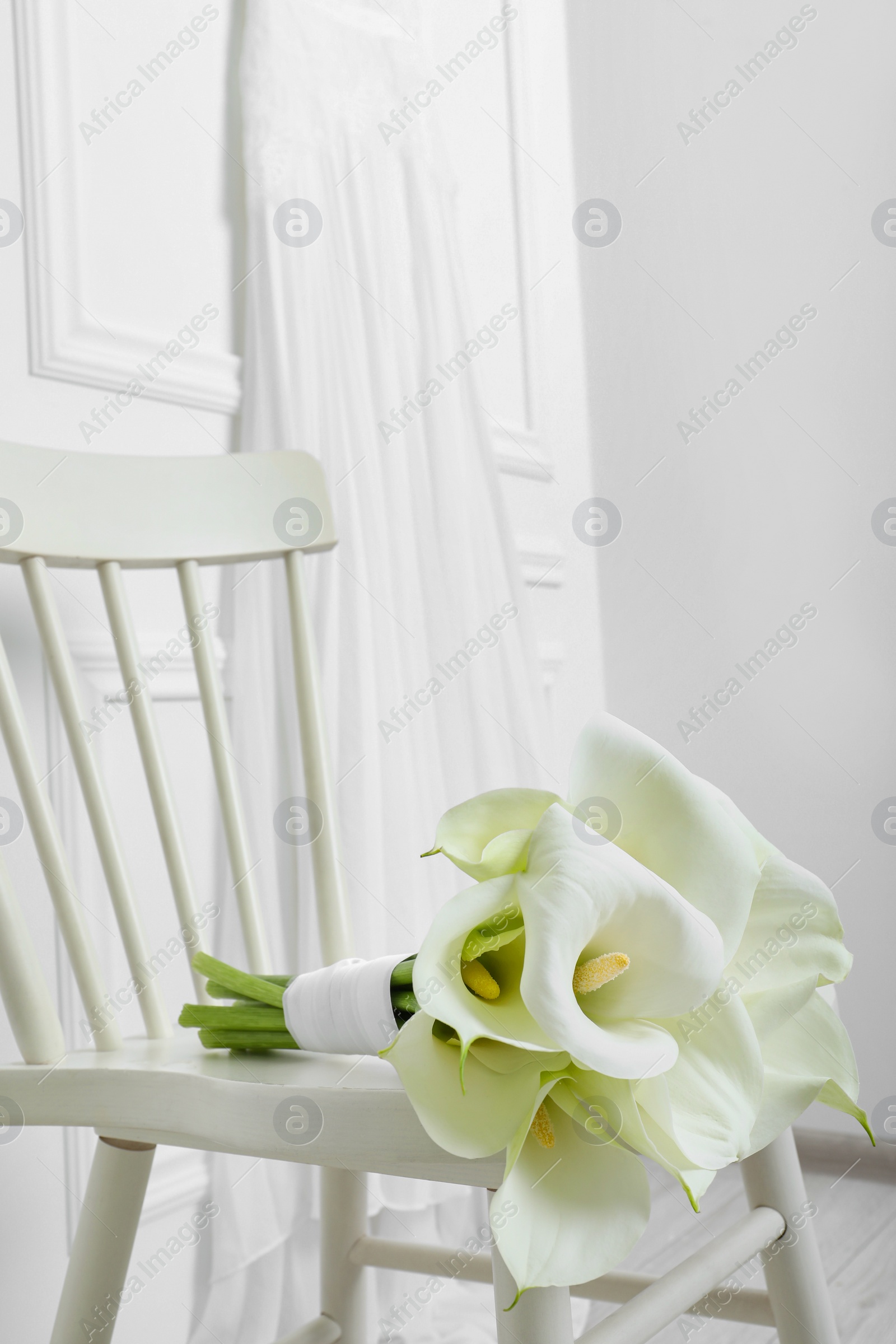 Photo of Beautiful calla lily flowers tied with ribbon on white chair indoors