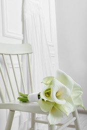 Beautiful calla lily flowers tied with ribbon on white chair indoors