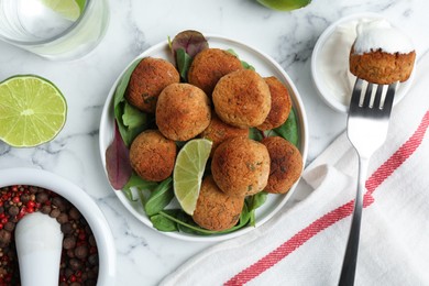 Photo of Delicious falafel balls with herbs and lime on white marble table, flat lay