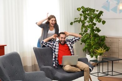 Emotional young couple with laptop celebrating victory at home