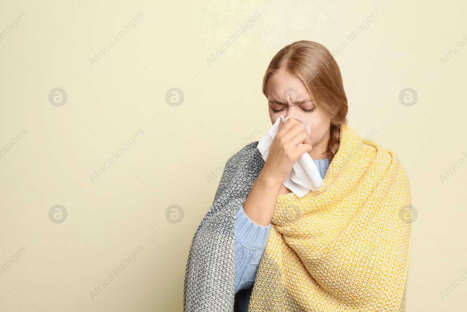 Image of Young woman wrapped in blanket sneezing on light background, space for text. Cold symptoms