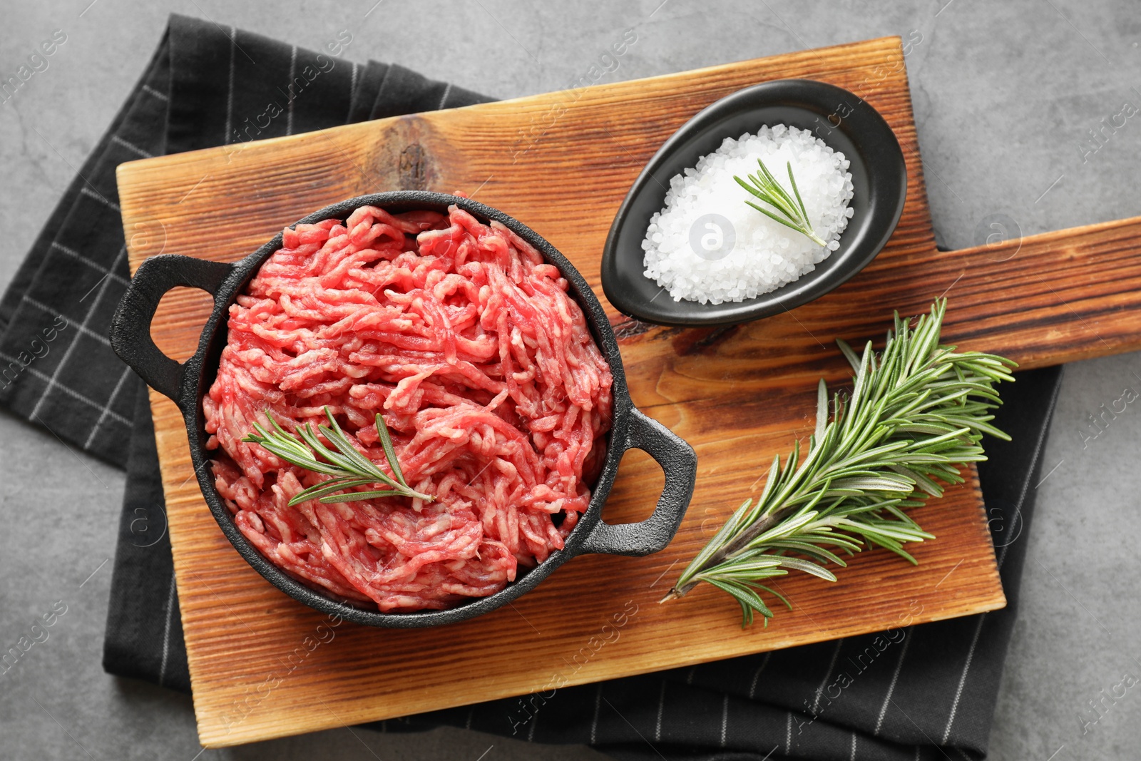 Photo of Raw ground meat in bowl, salt and rosemary on grey table, top view