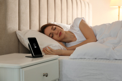 Photo of Smartphone charging on wireless pad and woman sleeping in bed