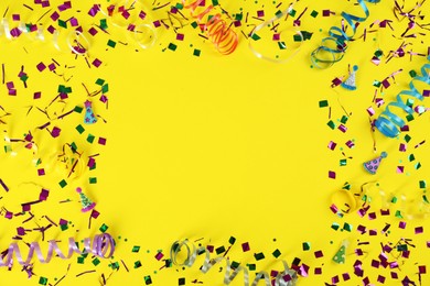 Photo of Frame of colorful serpentine streamers and confetti on yellow background, flat lay. Space for text