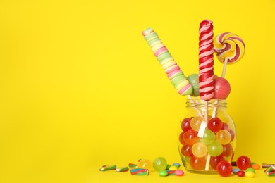 Photo of Jar with different delicious candies on yellow background. Space for text