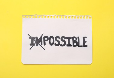 Photo of Motivation concept. Paper with changed word from Impossible into Possible by crossing over letters I and M on yellow background, top view